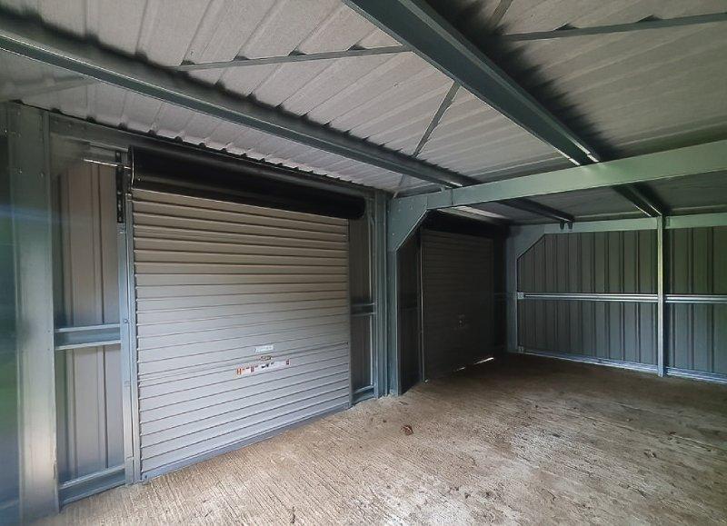 Interior view of a galvanized steel building frame featuring corrugated roofing and two grey roller shutter doors.