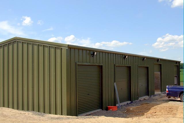 A green building with multiple closed roller doors and one slightly larger open roller door